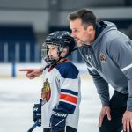 Youth hockey coach guiding a young player on an indoor ice rink, illustrating mental performance support in youth sports.