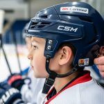 Close-up of a youth hockey helmet being adjusted by a parent or coach in an indoor arena setting.